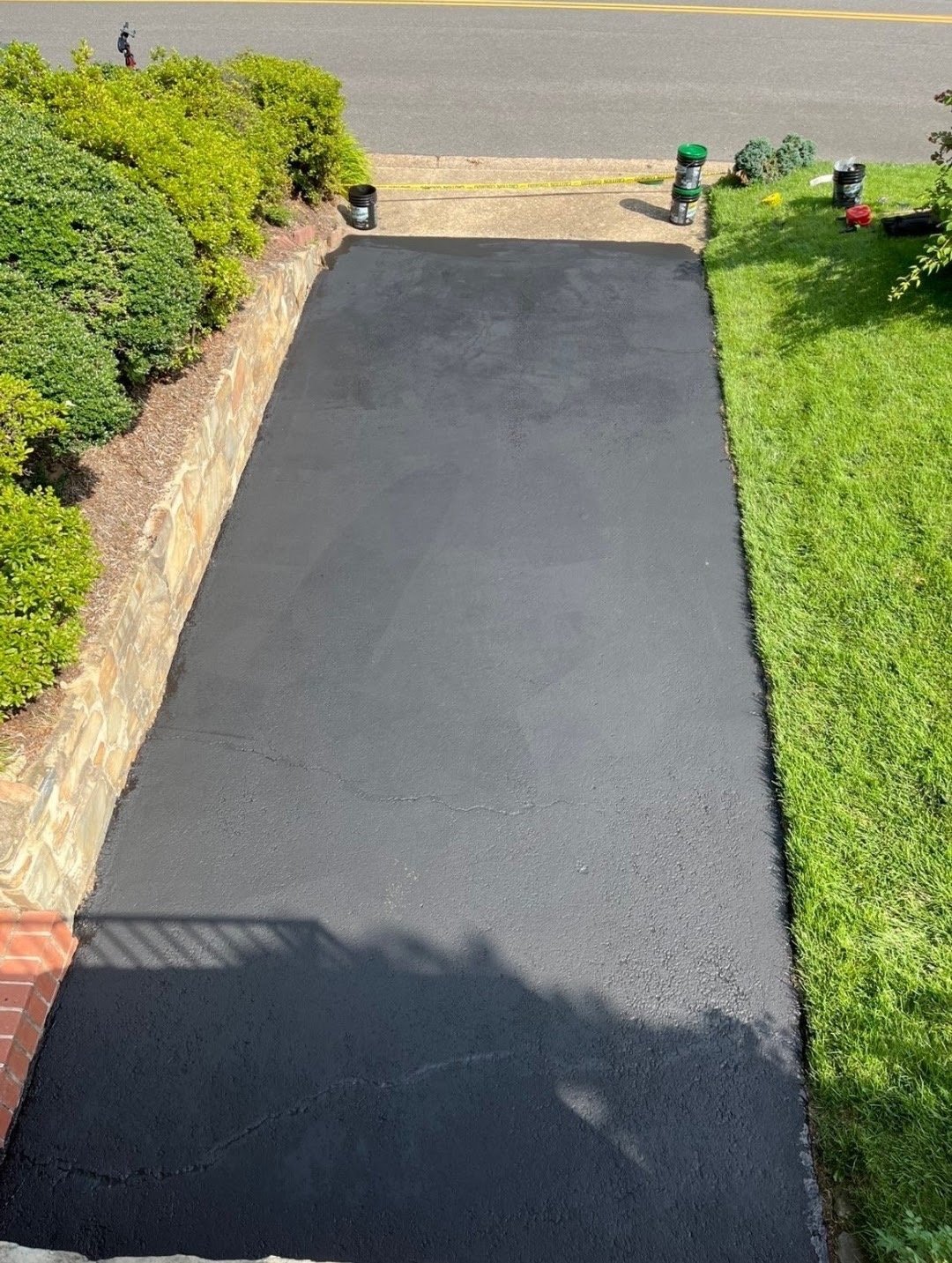 Aerial view of a newly paved black asphalt driveway bordered by green hedges and manicured lawns on either side